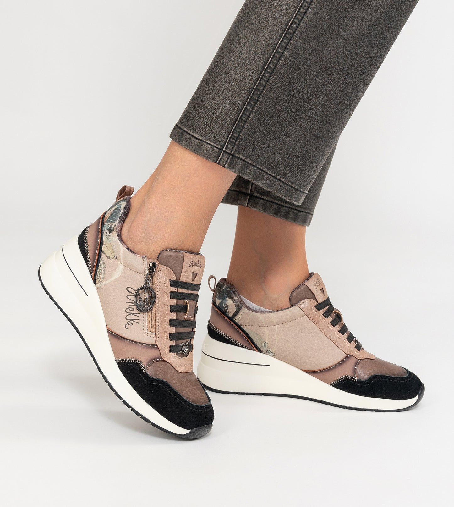 Zapatillas casual Anekke con cuña y cremallera lateral, en tonos neutros beig y negro, y detalles decorativos, diseño inspirado en la naturaleza.